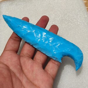 Könnte beinhalten: Ein helltürkises, handgehaltenes Werkzeug mit gebogenem Griff und spitzer Spitze. Das Werkzeug hat eine strukturierte Oberfläche und scheint aus einem festen Material zu bestehen. Das Objekt wird in der Hand einer Person gehalten.