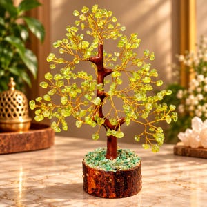 May include: A decorative tree sculpture featuring a dark brown trunk and thin gold wire branches adorned with small, translucent light green gemstone chips. The tree is set into a circular wooden base covered with green stone fragments.