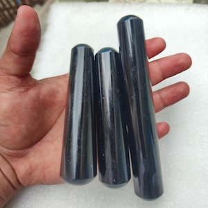 Puede incluir: Tres objetos cilíndricos de color azul oscuro con extremos redondeados se sostienen en una mano. Los objetos varían en longitud, con un acabado liso y brillante. Los artículos parecen estar hechos de un material sólido, posiblemente pulido.