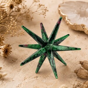 Può includere: Una scultura a forma di stella a più punte intagliata in zoisite verde con inclusioni di rubino magenta. L'oggetto presenta numerose punte affilate che si irradiano da un nucleo centrale, mostrando una texture naturale e levigata.