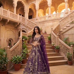 May include: A deep purple lehenga set featuring a long-sleeved blouse and a floor-length skirt, both adorned with intricate gold embroidery. A matching sheer purple dupatta is draped over one shoulder, completing the ensemble.