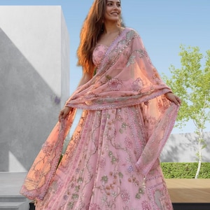 May include: A light pink lehenga with floral embroidery and a matching dupatta. The outfit features intricate detailing and embellishments. The word "Fashion" is visible in the top right corner.