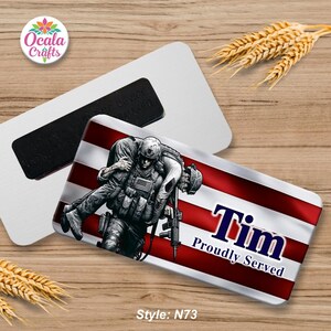 May include: A rectangular magnet with an illustration of a soldier carrying another soldier, set against a waving American flag. The name "Tim" and the phrase "Proudly Served" are displayed. The magnet is white with a black magnetic strip.