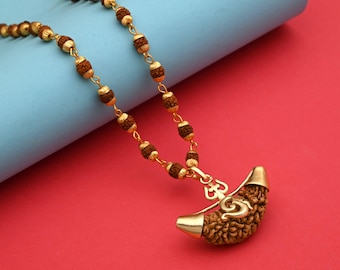 Puede incluir: Collar dorado con un colgante con un diseño texturizado en forma de media luna marrón y un dije dorado. El collar tiene una cadena de pequeñas cuentas marrones y eslabones dorados. El fondo es una combinación de rojo y azul.