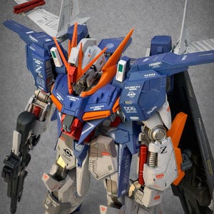 May include: A detailed model of a mecha robot, featuring a color scheme of blue, orange, gray, and white. The robot has intricate mechanical details, including wings, weapons, and various panels. The model is a collectible item.