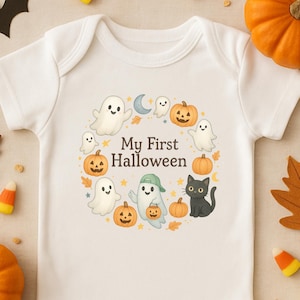 May include: White baby onesie with a Halloween-themed graphic. The design features smiling ghosts, pumpkins, a black cat, and the text "My First Halloween" in a circular arrangement. The onesie is made of soft material.