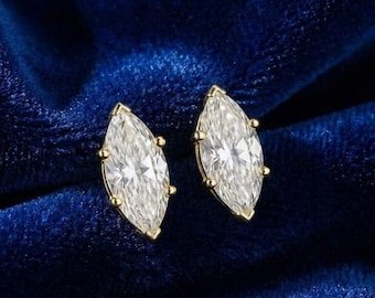 May include: A pair of marquise-cut diamond stud earrings with gold settings. The diamonds are clear and sparkling, set against a deep blue velvet background. The earrings are a classic jewelry item.