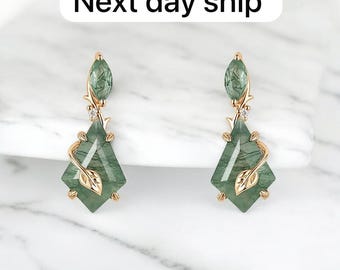May include: Gold-coloured earrings with green gemstone pendants. Each earring has a leaf design and a diamond-shaped green stone. The text "Next day ship" is at the top.