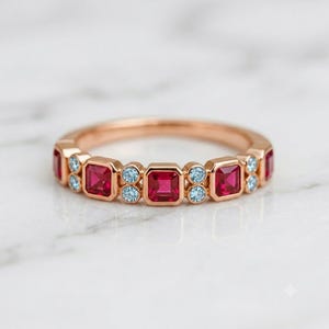 Peut inclure: Une bague en or rose présentant un motif répétitif de pierres précieuses rouge foncé de taille carrée alternant avec des paires de petites pierres précieuses rondes bleu clair, serties clos sur toute la circonférence de l'anneau en métal.