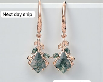May include: Rose gold earrings featuring a leaf design and green gemstone pendants. The earrings have a long hook and a textured leaf detail. The gemstones are a light green colour with darker green inclusions.