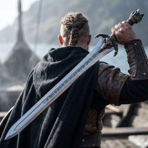 Peut inclure: Une longue épée en métal avec une garde détaillée et des runes gravées le long de la lame. L'épée est tenue sur l'épaule, présentant un pommeau sombre et usé ainsi qu'une garde en forme de tête de créature, avec une pointe acérée.