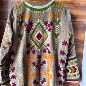 Puede incluir: Chaqueta de terciopelo color beige con intrincados bordados en tonos verdes, naranjas y burdeos. El dise&ntilde;o presenta patrones florales y geom&eacute;tricos, con un motivo en forma de diamante en la espalda. La chaqueta tiene mangas largas y cuello.