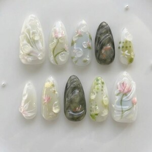 May include: A set of ten artificial nails with a floral design. The nails are oval-shaped and feature a variety of designs, including pink flowers, green leaves, and swirling patterns. The nails are in shades of white, green, and gray.