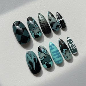 May include: A set of ten artificial nails in various shapes and designs. The nails feature a color palette of teal, black, and gray. Designs include checkered patterns, flame motifs, and abstract shapes. Some nails have a matte finish, while others are glossy.
