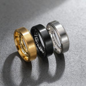 Puede incluir: Se muestran tres anillos en oro, negro y plata. El anillo dorado tiene la inscripción "my dream love", el anillo negro dice "I Love You" y el anillo plateado dice "Forever in my heart".
