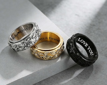 May include: Three engraved spinner rings in silver, gold, and black. The silver ring has the inscription "Jaytie 03/03/23". The gold ring says "Always & Forever". The black ring says "LOVE YOU". Each ring features an eye-shaped pattern.