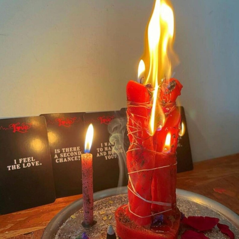 A red candle is burning on a table, with smoke rising from it. In the background, there are three black cards with white text, but the text is not clear enough to transcribe accurately.