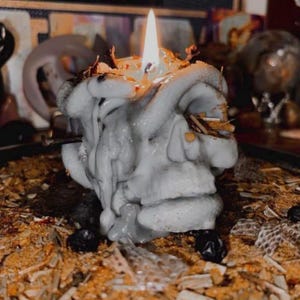 A white candle with a flame burning on top, surrounded by various objects, including a skull-shaped candle holder and a wooden surface.