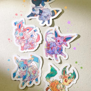 May include: Five holographic stickers featuring cartoon characters in various colours. The stickers depict creatures with floral and decorative elements, in shades of blue, pink, purple, green, and orange.