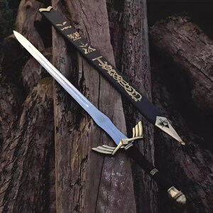 Puede incluir: Una espada decorativa con una hoja plateada y detalles dorados en la guarda y el mango. El mango negro est&aacute; detallado con bandas doradas. La espada descansa sobre una superficie de madera junto a su vaina negra, con patrones dorados.