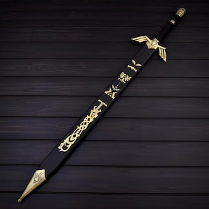 Puede incluir: Una espada decorativa negra y dorada con dise&ntilde;os intrincados. La espada presenta una empu&ntilde;adura y detalles de la hoja dorados, con s&iacute;mbolos y patrones a lo largo de la hoja. Se muestra sobre una superficie de madera oscura.