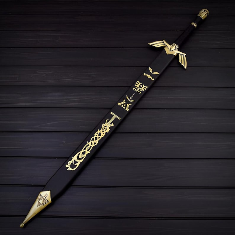 Puede incluir: Una espada decorativa negra y dorada con dise&ntilde;os intrincados. La espada presenta una empu&ntilde;adura y detalles de la hoja dorados, con s&iacute;mbolos y patrones a lo largo de la hoja. Se muestra sobre una superficie de madera oscura.
