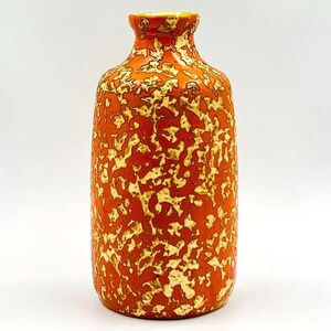Può includere: Un vaso alto in ceramica con un motivo maculato. Il vaso è principalmente arancione con un motivo irregolare color crema. Il bordo e l'interno del vaso sono di colore giallo chiaro. Il vaso ha una forma cilindrica con un bordo leggermente svasato.