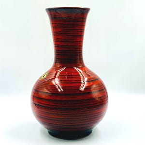 Può includere: Un vaso decorativo con un corpo bulboso e un collo sottile. Il vaso presenta un motivo a righe rosse e nere, con una finitura lucida. La base è nera e una piccola etichetta oro e verde è visibile.