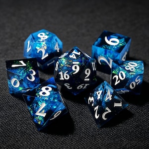Pode incluir: Um conjunto de sete dados poliédricos feitos de resina azul translúcida com flocos de folha iridescente verde e azul incrustados. Cada dado apresenta bordas afiadas e números gravados em branco, incluindo um d20, d12, d10, d8, d6, d4 e um dado de percentagem.