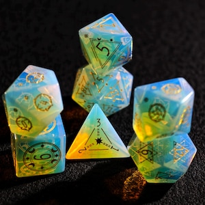 May include: A set of iridescent polyhedral dice in shades of blue, yellow, and green. The dice feature gold-colored symbols and numbers. The set includes a variety of shapes, including a triangular die and a multi-sided die.
