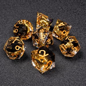 Puede incluir: Un conjunto de siete dados poliédricos para juegos de rol. Están hechos de resina transparente con interior negro y números dorados. El conjunto incluye un d4, d6, d8, d10, d12, d20 y un dado de porcentaje.