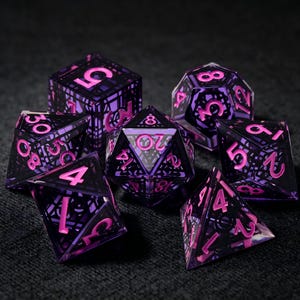 Peut inclure: Un ensemble de sept dés polyédriques dotés d'une coque en résine violette translucide avec une structure interne noire complexe et des chiffres rose vif. La collection comprend un d20, d12, d10, d8, d6, d4 et un dé de pourcentage, tous aux arêtes vives et aux chiffres clairs.