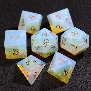Op de afbeelding: Set van zeven opalescente polyhedrale dobbelstenen voor tabletopspellen. De dobbelstenen zijn een mix van blauw en geel, met bruine cijfers. Inclusief een D4, D6, D8, D10, D12, D20 en een percentagedobbelsteen.