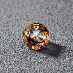 May include: A multi-faceted, clear resin D20 die with gold numbering. The interior features a mix of red, gold, and blue inclusions, creating a galaxy-like effect. The die is designed for tabletop role-playing games.