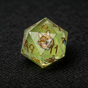 Può includere: Un dado a venti facce realizzato in resina verde lime traslucida con glitter dorati incorporati. Il dado presenta numeri color oro e piccole illustrazioni di un cane corgi e impronte di zampe sulle facce. Il numero venti è sostituito da un corgi.