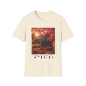 May include: Off-white t-shirt displaying a rectangular image of a Japanese landscape with red and orange autumn leaves, a temple, and the word "KYOTO" in black letters beneath the image.