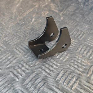 Könnte beinhalten: Eine mattschwarze Metallhalterung mit einer U-förmigen Basis, die ein einzelnes kreisförmiges Loch aufweist, sowie zwei nach oben ragenden Seitenarmen, die jeweils mit einer kreisförmigen Bohrung versehen sind. Das Bauteil hat eine glatte Oberfläche.