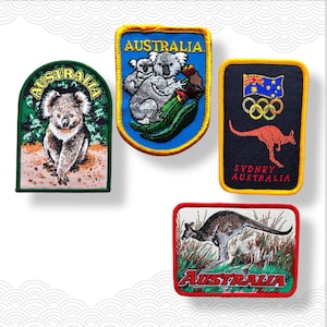 May include: Four embroidered patches with Australian designs. One patch shows a koala bear, another depicts koalas with eucalyptus leaves, a third has the Olympic rings and a kangaroo, and the last one shows a kangaroo in a grassy field.