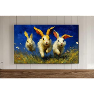 May include: A canvas print depicting three running rabbits. The rabbits have white fur with yellow and orange ears, set against a blue background. The artwork has a painterly style, with visible brushstrokes and a vibrant colour palette. The rabbits are depicted in a field of grass and small white flowers.