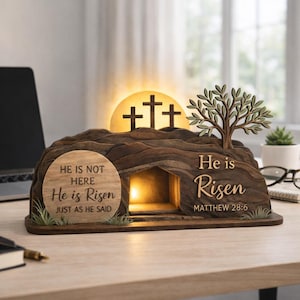 Puede incluir: Decoración de Pascua de madera que representa la tumba vacía con una luz interior. La escena incluye tres cruces, un árbol y el texto "He is Risen" y "He is not here, He is Risen, just as He said."