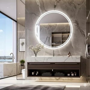 Op de afbeelding: Moderne badkamer met een grote, ronde, verlichte spiegel boven een donkere houten wastafel met een marmeren aanrechtblad. De wastafel heeft twee lades en open schappen. Een groot raam biedt uitzicht op de stad.