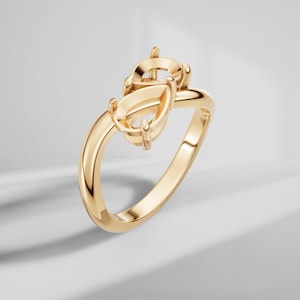 May include: A polished gold ring featuring a pear-shaped setting designed to hold a gemstone. The ring has a smooth, rounded band and a prong setting that extends upward from the center, showcasing a metallic finish with reflective highlights.