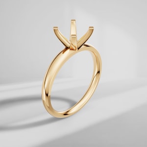 May include: A polished yellow gold ring setting featuring a four-prong head designed to hold a single gemstone. The band is smooth and circular, showcasing a reflective metallic finish with clean lines and a minimalist structural design.