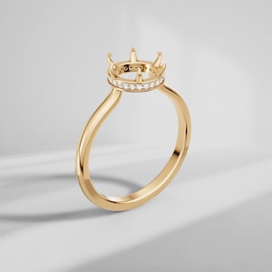 May include: A gold ring setting featuring a circular head with six pointed prongs designed to hold a gemstone. The base of the head is encircled by a row of small, clear, round-cut pavé diamonds, set into the polished yellow gold band structure.