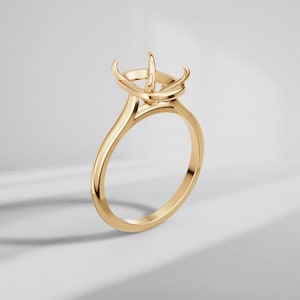 May include: A polished gold ring setting featuring a four-prong head designed to hold a single gemstone. The band is smooth and rounded, transitioning into a tapered shank that supports the elevated prong structure at the top of the ring.