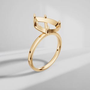 May include: A gold ring with a pear-shaped setting. The ring features a slender band and a setting with four prongs. The ring is made of shiny gold and is set against a white background.