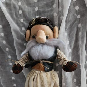 May include: A handmade doll with a whimsical design. The doll features a large nose, white beard, and is dressed in striped pants, a black vest, and brown shoes. The doll is approximately 10 inches tall.