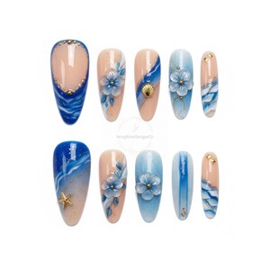 Könnte beinhalten: Ein Set aus zehn künstlichen Nägeln mit Designs zum Thema Ozean. Die Nägel zeigen Blau-, Weiß- und Goldtöne mit Akzenten wie Muscheln, Seesternen und floralen Verzierungen. Einige Nägel haben eine nackte Basis mit detaillierten Kunstwerken.