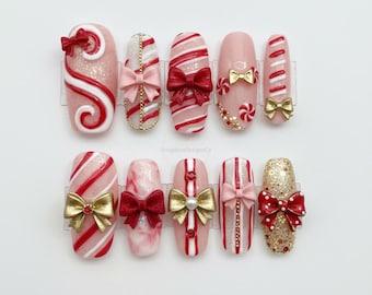 May include: A collection of ten artificial nails with festive designs. The nails feature red and white stripes, bows, and glitter accents. Some nails have candy cane swirls, while others have gold or pink bows.