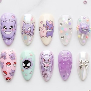 May include: A set of ten almond-shaped artificial nails with various designs. The designs include cartoon characters, patterns, and embellishments in shades of purple, pink, and white. Some nails feature the text "SWEET GIRL".